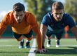 Zwei Amateur-Fußballspieler führen auf einem grünen Spielfeld Liegestütze als Teil eines Kraftausdauertrainings durch, zeigen Action, Fokus und Teamgeist.